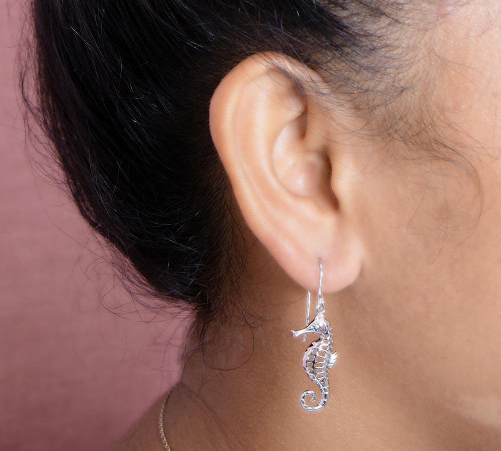 The picture shows a model wearing a 925 sterling silver seahorse hook earring with topaz.