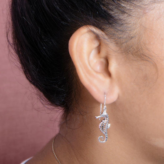 The picture shows a model wearing a 925 sterling silver seahorse hook earring with topaz.