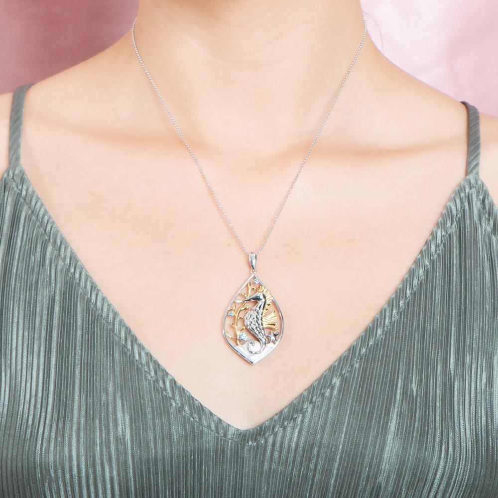 The picture shows a model wearing a two-tone white and yellow gold sea horse mandorla pendant with aquamarine and topaz.