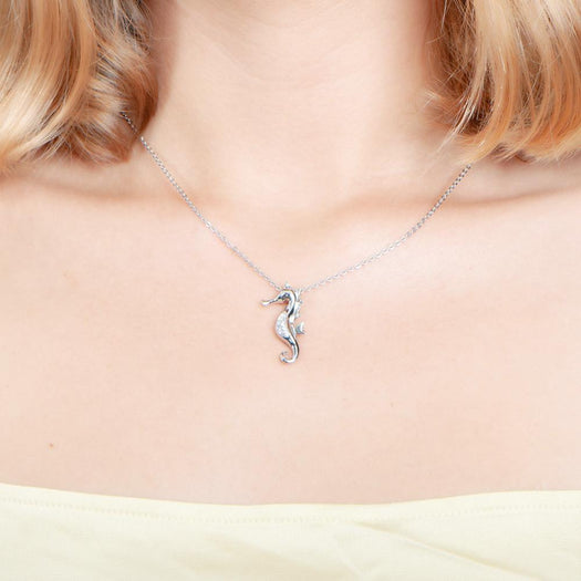 In this photo there is a model with blonde hair and a yellow shirt wearing a sterling silver seahorse pendant with topaz.