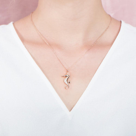 In this photo there is a model with a white shirt, wearing a rose gold seahorse pendant with topaz gemstones.