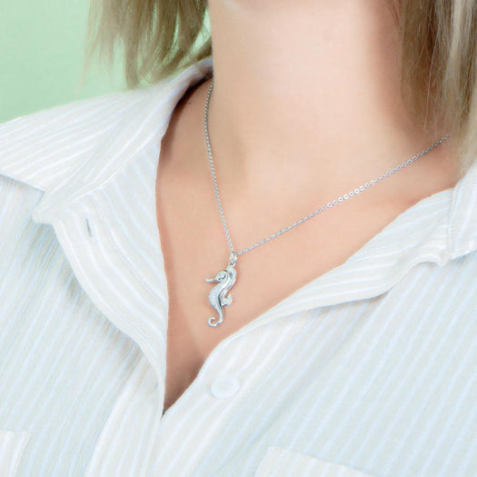 In this photo there is a model turned to the left with blonde hair and a tan and white striped shirt, wearing a white gold seahorse pendant with topaz gemstones.