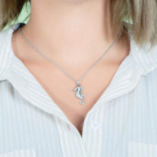 In this photo there is a model with blonde hair and a tan and white striped shirt, wearing a white gold seahorse pendant with topaz gemstones.