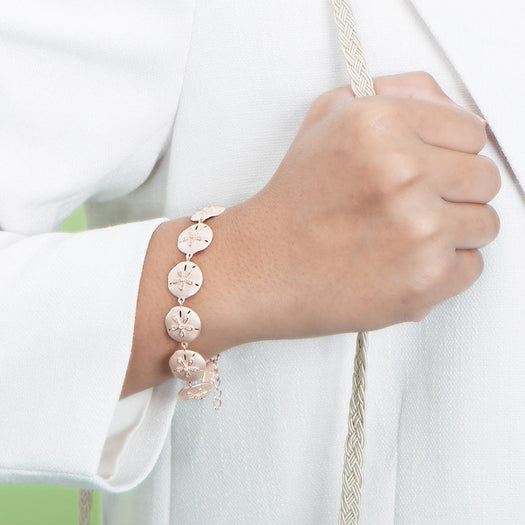 The picture shows a model wearing a rose gold sand dollar bracelet with topaz.