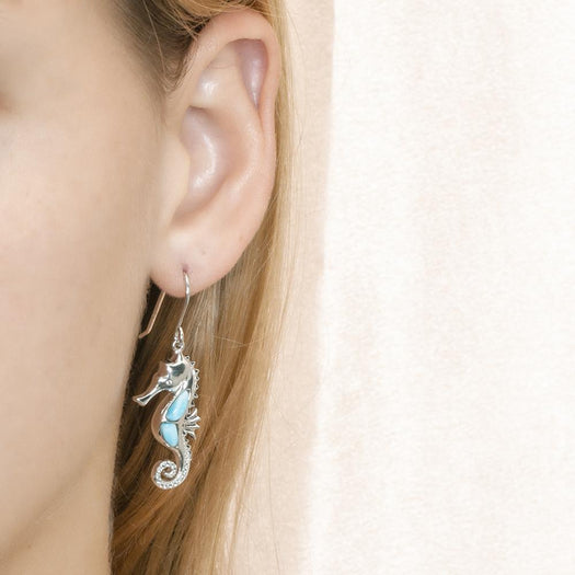 The picture shows a model wearing a 925 sterling silver larimar seahorse hook earring with topaz.