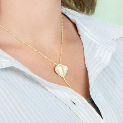 The picture shows a model wearing a yellow gold manta ray pendant with topaz.