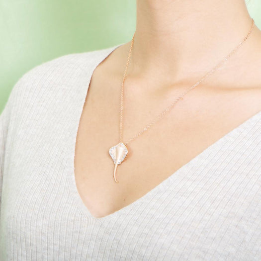 The picture shows a model wearing a rose gold manta ray pendant with topaz.