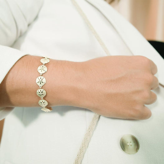 The picture shows a model wearing a yellow gold sand dollar bracelet with topaz