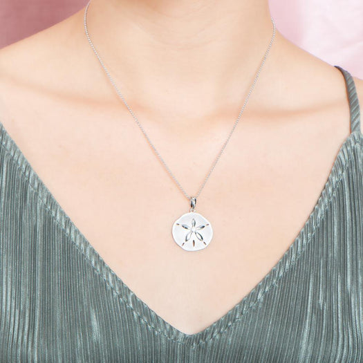 The picture shows a model wearing a white gold sand dollar pendant with topaz.