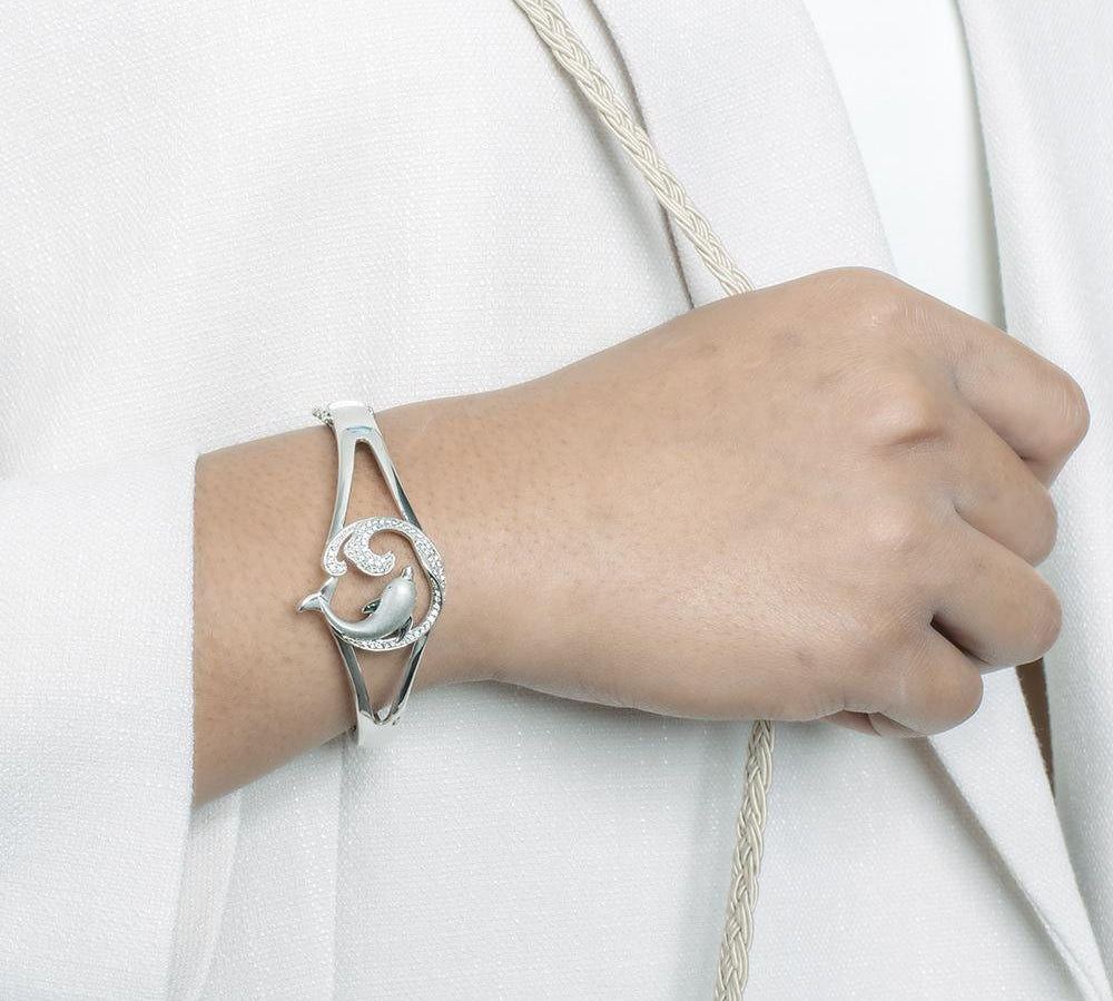 The picture shows a model wearing a 925 sterling silver dolphin and wave bangle with topaz.