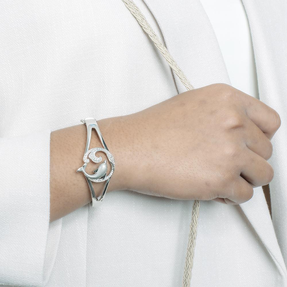 The picture shows a model wearing a 925 sterling silver dolphin and wave bangle with topaz.
