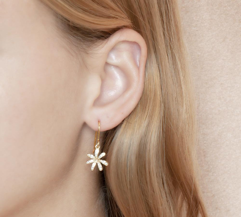 In this photo there is a model with blonde hair in profile, wearing yellow gold tiare gardenia dangle earrings with topaz gemstones.