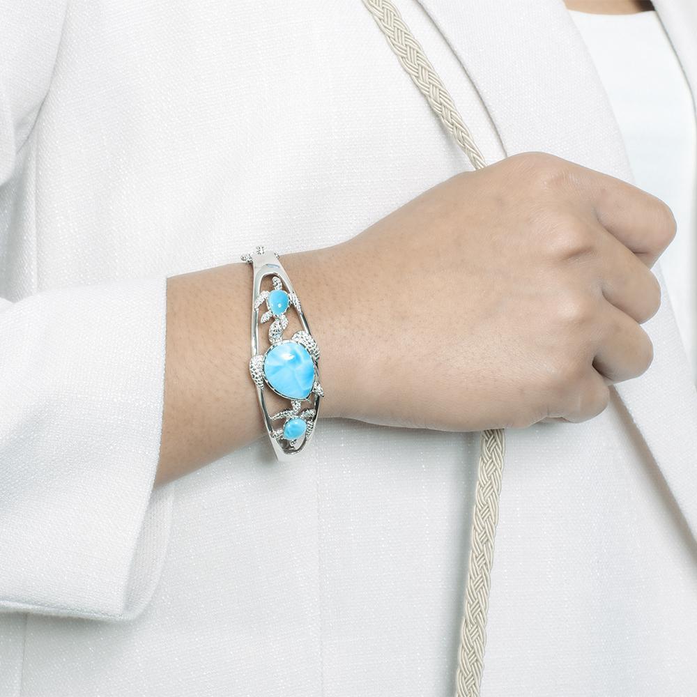 The picture shows a model wearing a 925 sterling silver three sea turtle bracelet with three larimar gemstones.